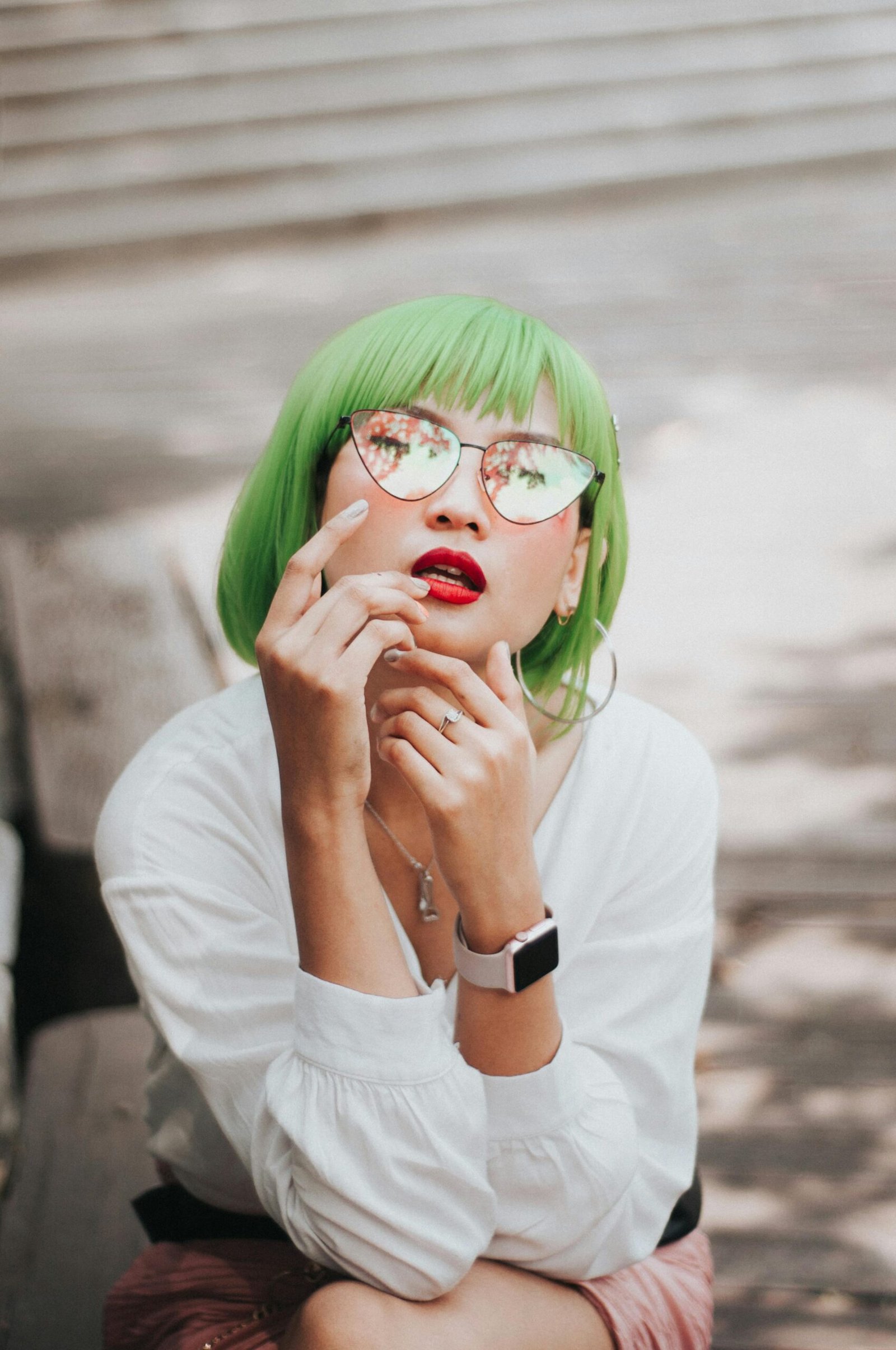 Portrait of a stylish woman with green hair and sunglasses posing outdoors.